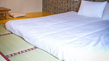 A neatly made bed with white bedding, a wooden nightstand, and a tatami mat.