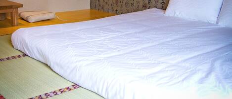 A neatly made bed with white bedding, a wooden nightstand, and a tatami mat.