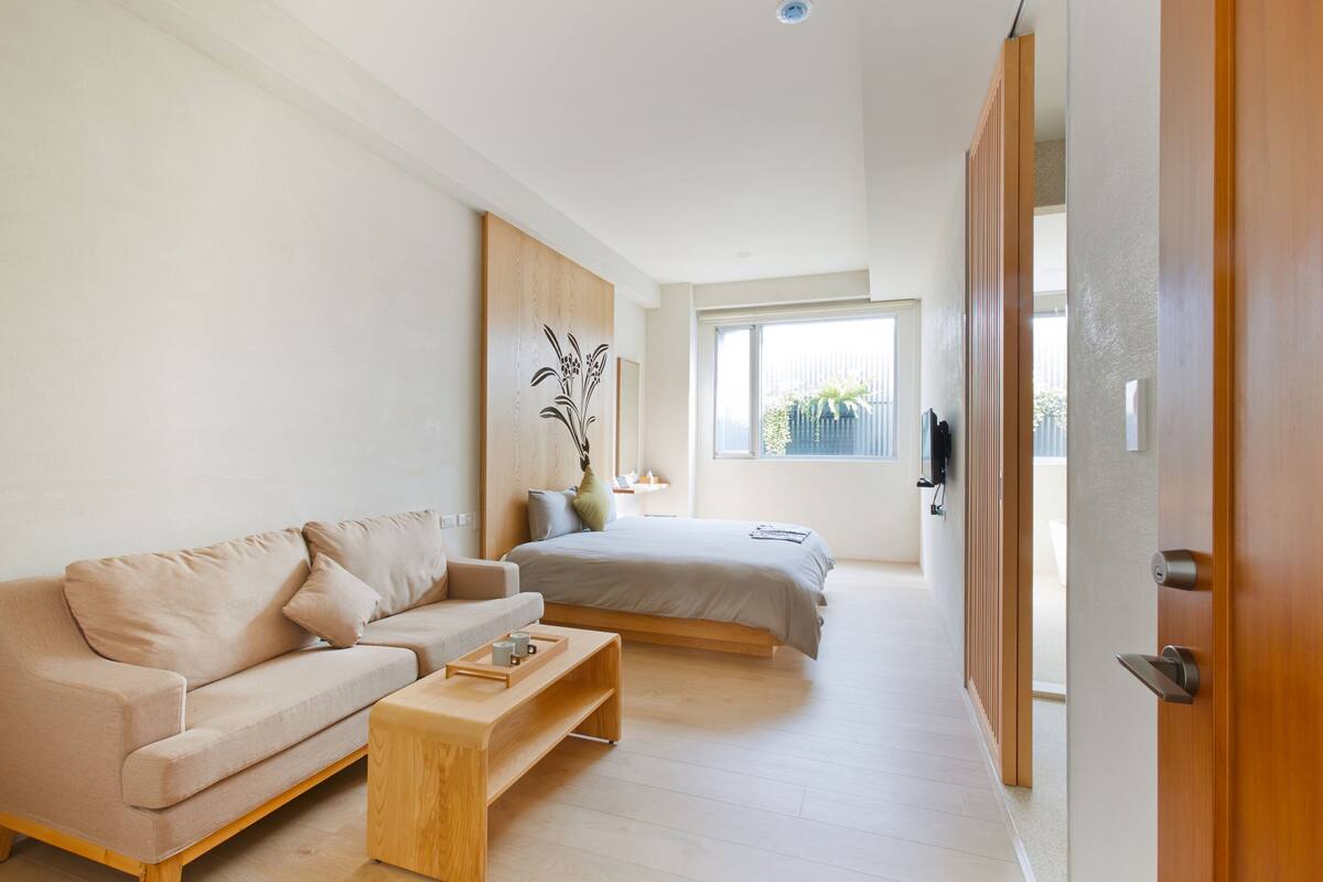 Un dormitorio moderno y minimalista con cama, sofá y una mesita de madera.