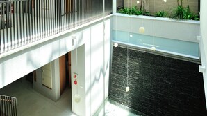 Un atrium à plusieurs niveaux, doté d’un élément décoratif central avec de l’eau, de garde-corps en bois et de plantes suspendues.