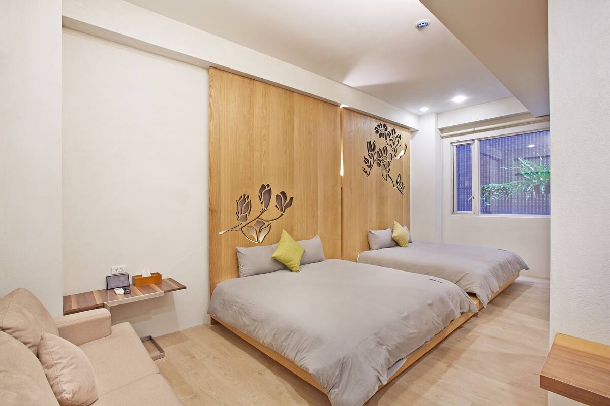 Un dormitorio moderno con dos camas, un cabecero de madera, un escritorio pequeño y una ventana con vistas a zonas verdes.