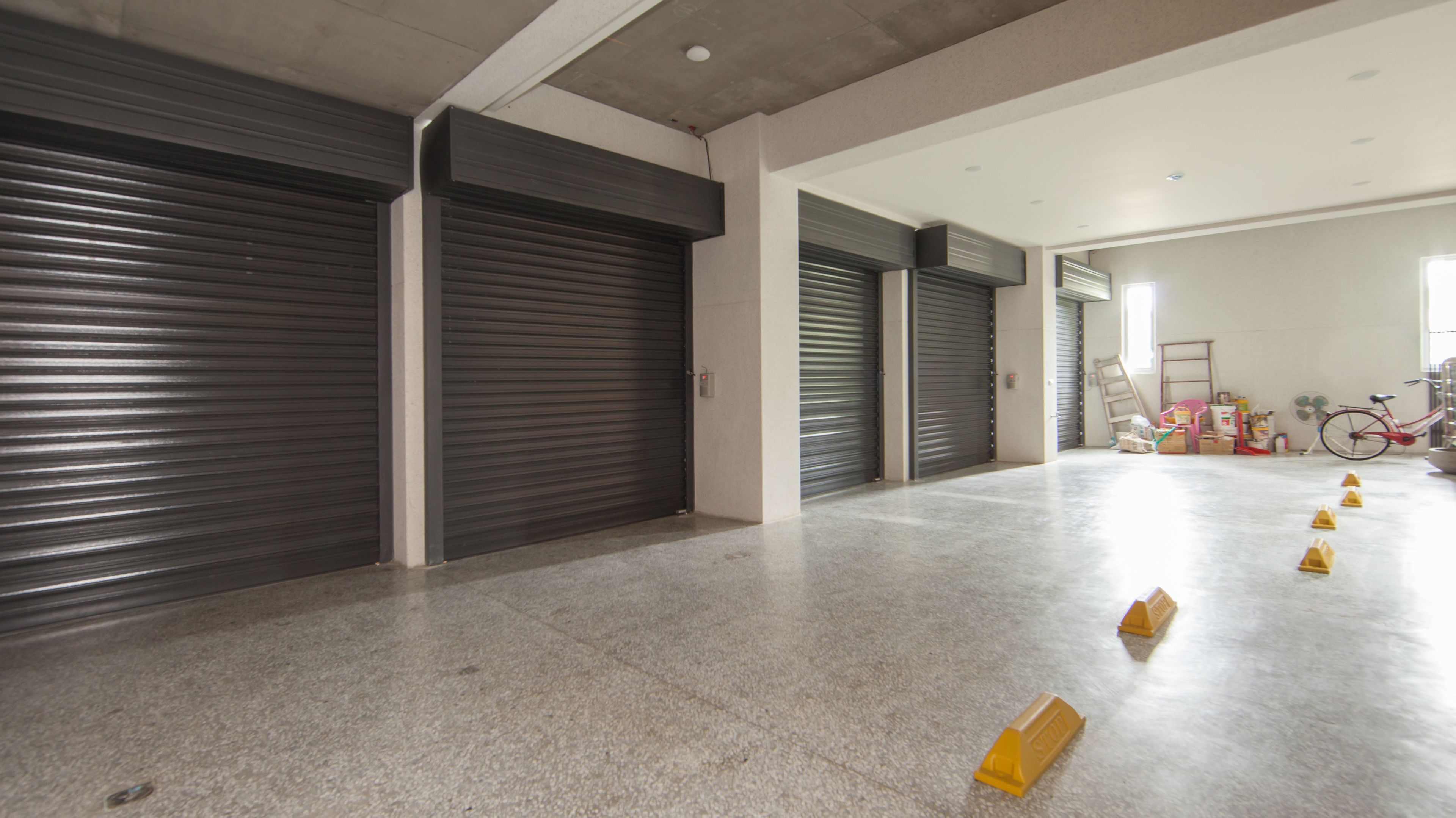 A spacious hallway with closed metal shutters, a concrete floor, and a bicycle in the background.