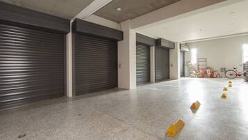A spacious hallway with closed metal shutters, a concrete floor, and a bicycle in the background.