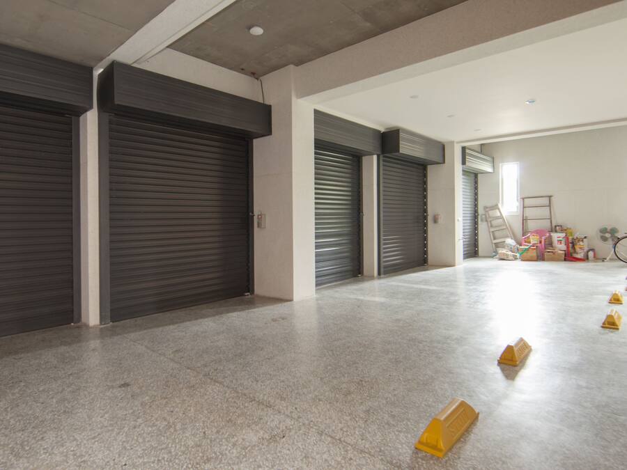 A spacious hallway with closed metal shutters, a concrete floor, and a bicycle in the background.