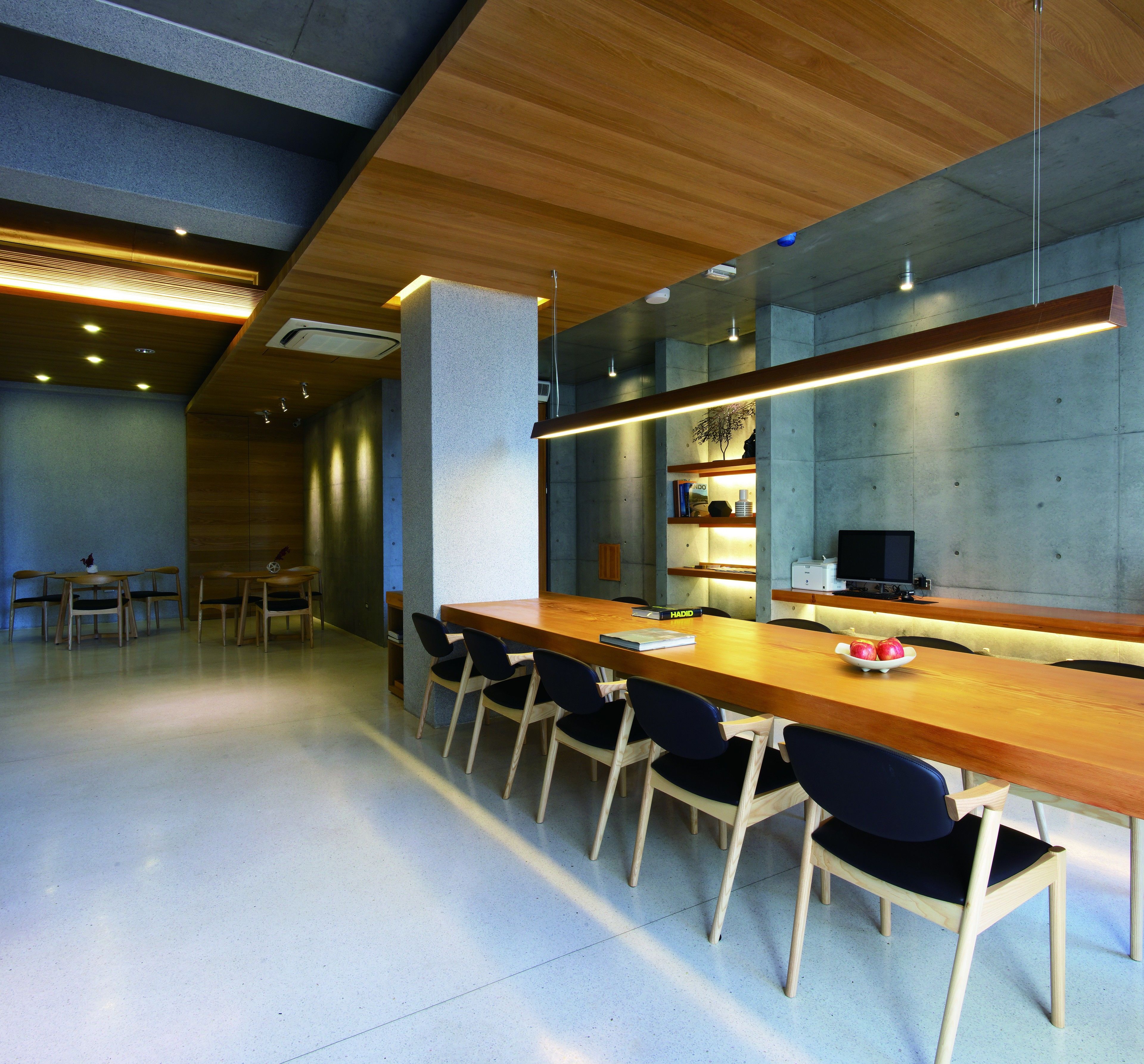 A modern conference room with a long wooden table, black chairs, and built-in shelves with books and decorative items.