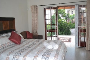A bedroom with a bed, pillows, and a view through a sliding glass door to an outdoor area with greenery. - Cycad Lodge (East London)
