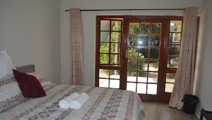 A bedroom with a bed, curtains, a window, and a door leading to an outdoor area. - Cycad Lodge (East London)