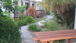 A wooden bench in a garden area with a pathway leading to a building. - Cycad Lodge (East London)