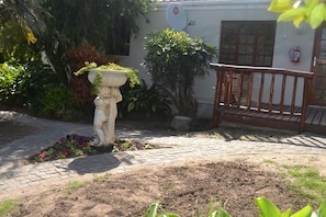 Um jardim com um banco de madeira, um cachepot de pedra e diversas plantas.