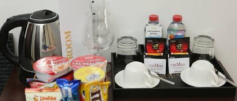A hotel room's breakfast setup with a kettle, coffee, tea, and various food items on a tray.