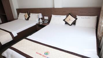 A hotel room with two beds, each with a wooden headboard and white bedding. There are pillows with the hotel's logo and name, a bedside table with a lamp, and a phone.