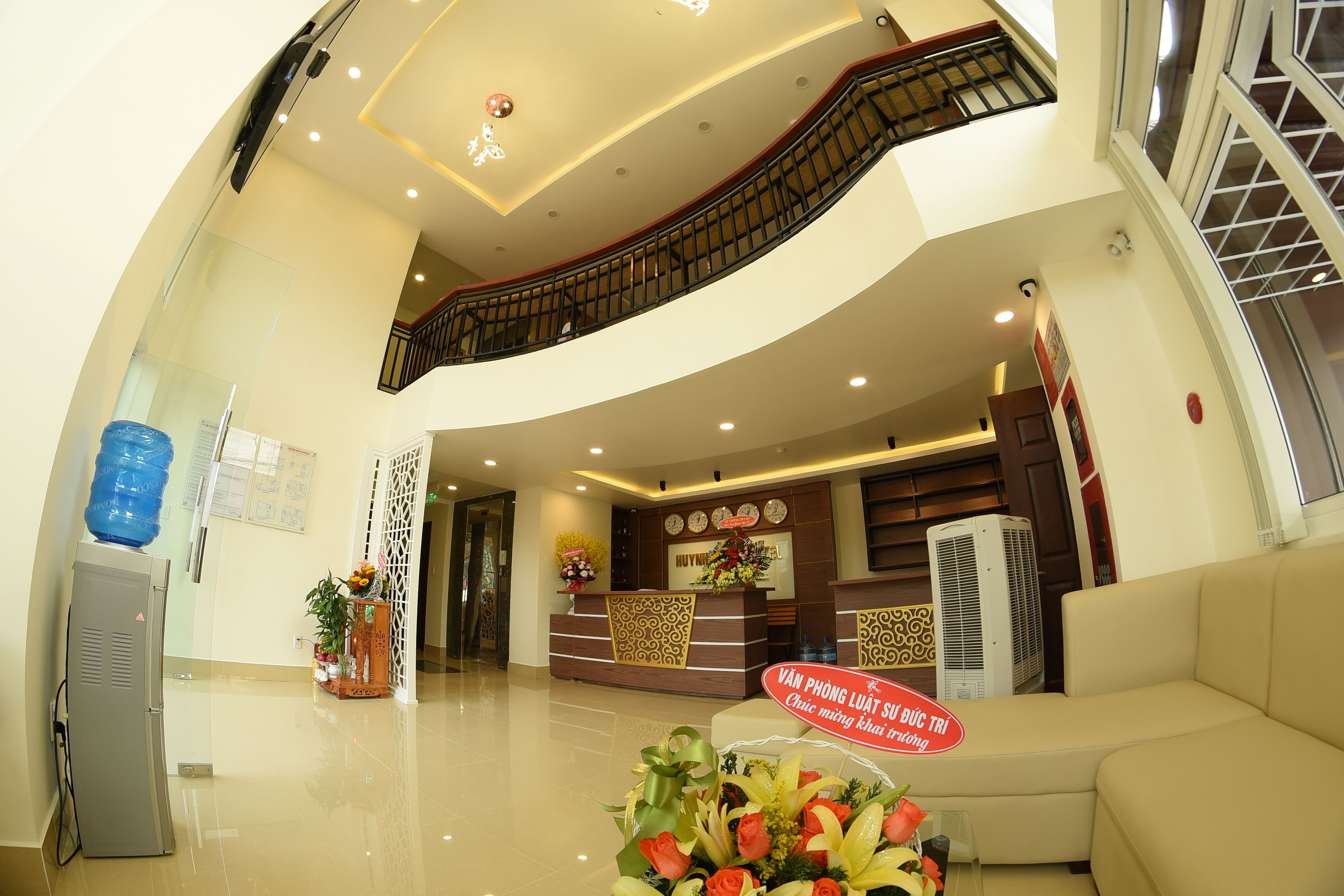A hotel reception area with a reception desk, a staircase, and a water dispenser.