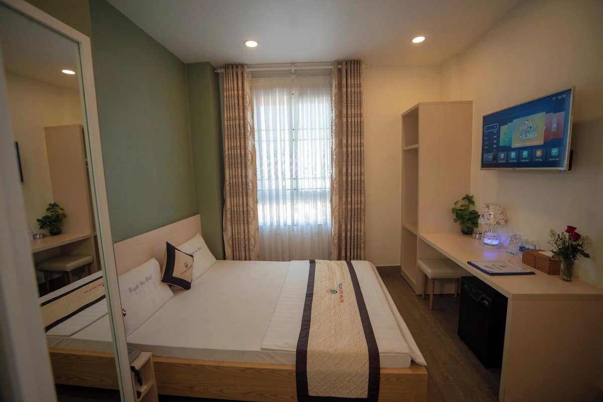 Une chambre d’hôtel équipée d’un lit, d’un bureau, d’une chaise, d’une télévision et d’une fenêtre avec des rideaux.