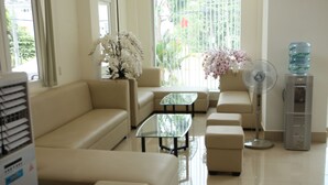 A modern living room with a beige sofa, a glass coffee table, and a water dispenser. - Huynh Duc 2 Hotel (Cao Lanh)