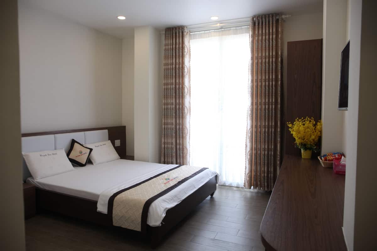 Une chambre d’hôtel avec un grand lit, une table de chevet en bois, un bureau agrémenté d’un vase de fleurs et une armoire.