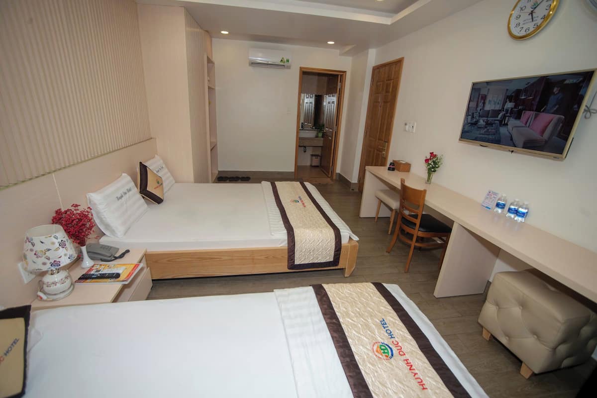 Une chambre d’hôtel avec deux lits, un bureau, une chaise, une télévision et une horloge au mur.