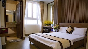 A hotel room with a large bed, a wooden headboard, a bedside table with a vase of flowers, and a bathroom visible through an open door. - Huynh Duc 2 Hotel (Cao Lanh)