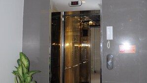 Un ascensor con pantalla digital, teléfono en la pared y una planta en maceta.