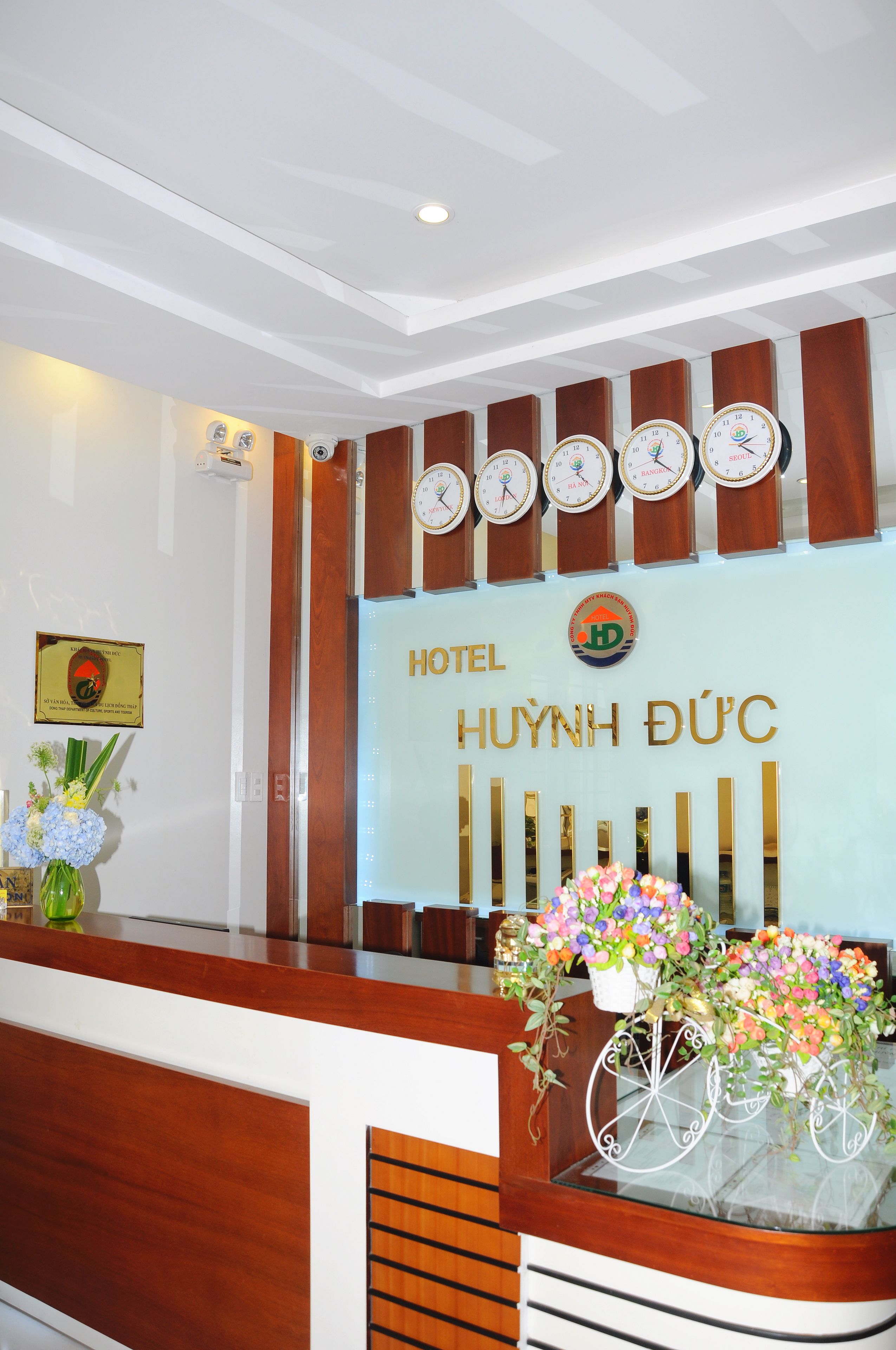 A hotel reception desk with clocks, a logo, and a floral arrangement.