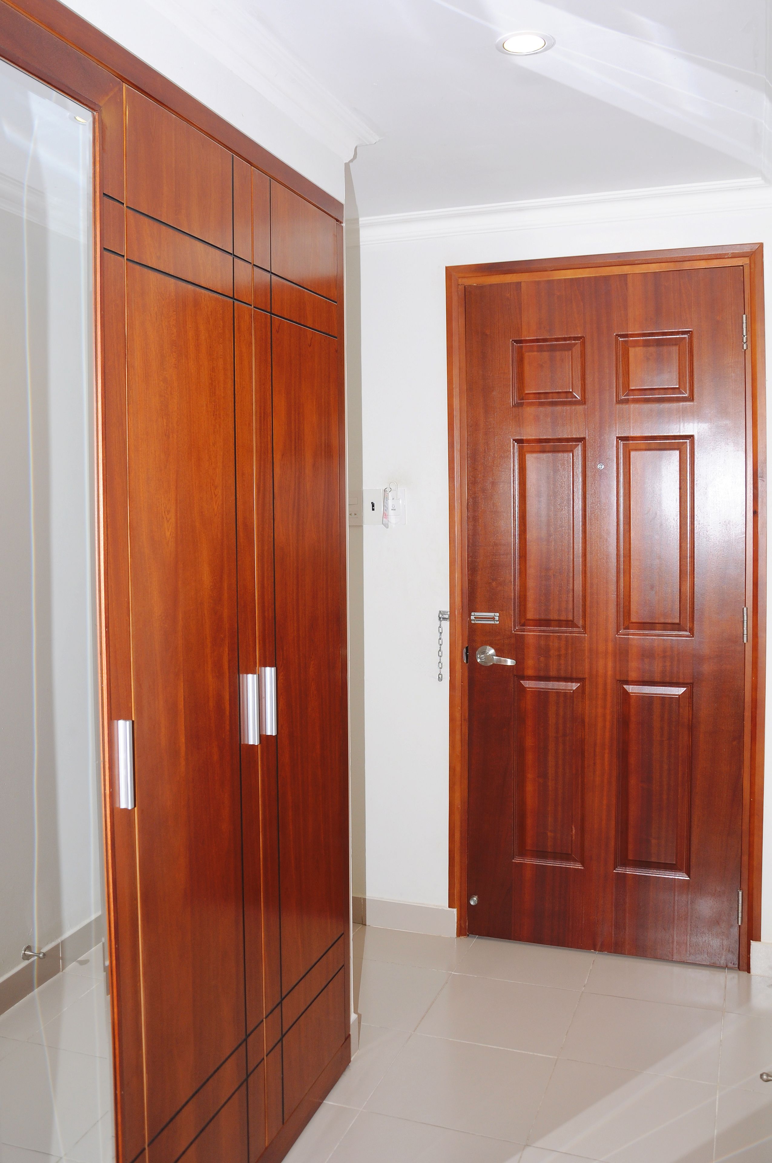 Una habitación con un armario de madera, una puerta de madera y suelo de baldosas.