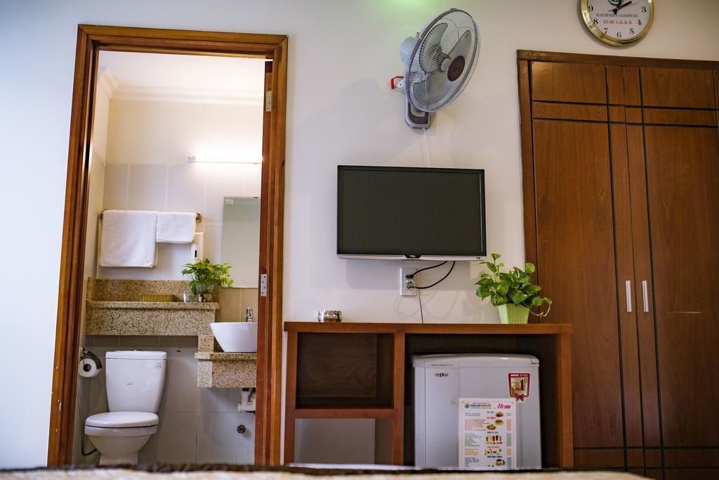 A bathroom with a toilet, sink, mirror, and a television mounted on the wall.