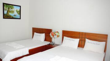 A hotel room with two beds, each with a wooden headboard and white bedding. There is a framed picture on the wall and a vase with flowers on the nightstand.