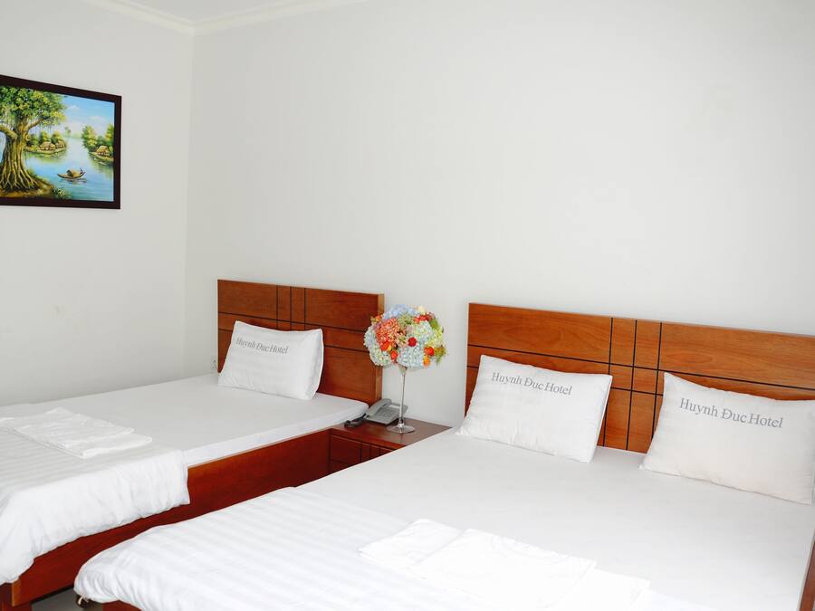 A hotel room with two beds, each with a wooden headboard and white bedding. There is a framed picture on the wall and a vase with flowers on the nightstand.