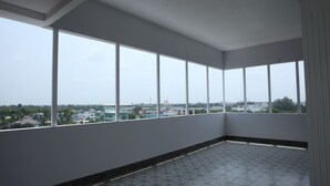 Una habitación con ventanas amplias, piso de baldosas y vistas a edificios y árboles.