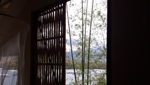 A window with a bamboo screen, a view of a river, and some greenery. - Bahay Isla Sanctuario (Puerto Galera)