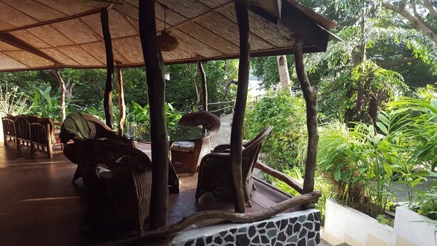 An outdoor covered seating area with wicker furniture and a stone wall. - Bahay Isla Sanctuario (Puerto Galera)