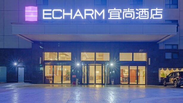 The exterior of ECHARM hotel with a prominent illuminated sign, large glass doors, and a parking area in front. - Echarm Hotel Shanghai Hongqiao Airport (Shanghai)