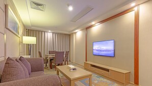 A hotel room with a sofa, a coffee table, a TV on the wall, a dining area with chairs, and a carpeted floor. - Echarm Hotel Shanghai Hongqiao Airport (Shanghai)