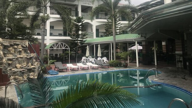 A hotel with a pool area, lounge chairs, and palm trees.