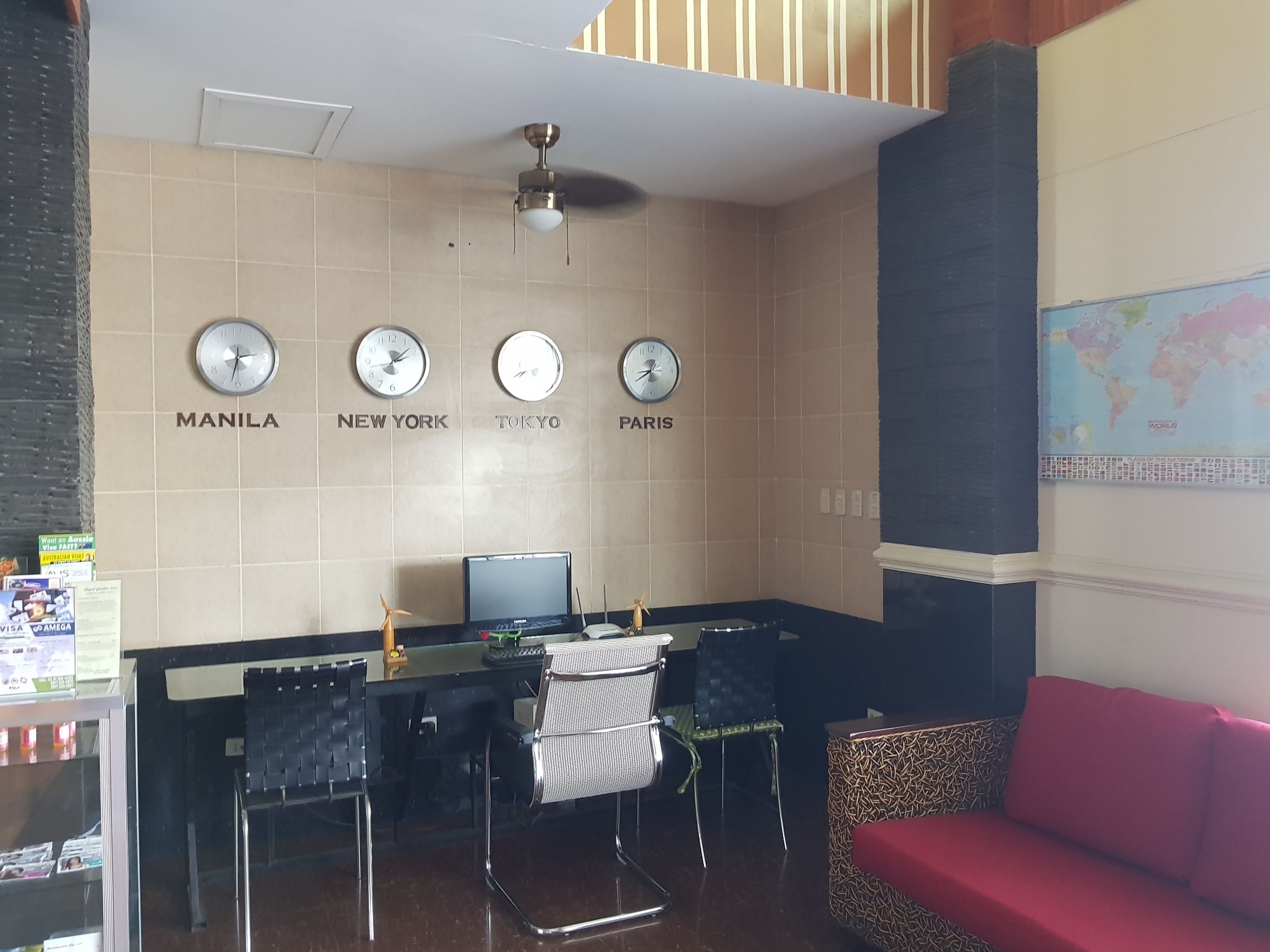 A hotel lobby with a reception desk, a seating area with a red sofa, and clocks indicating different cities.