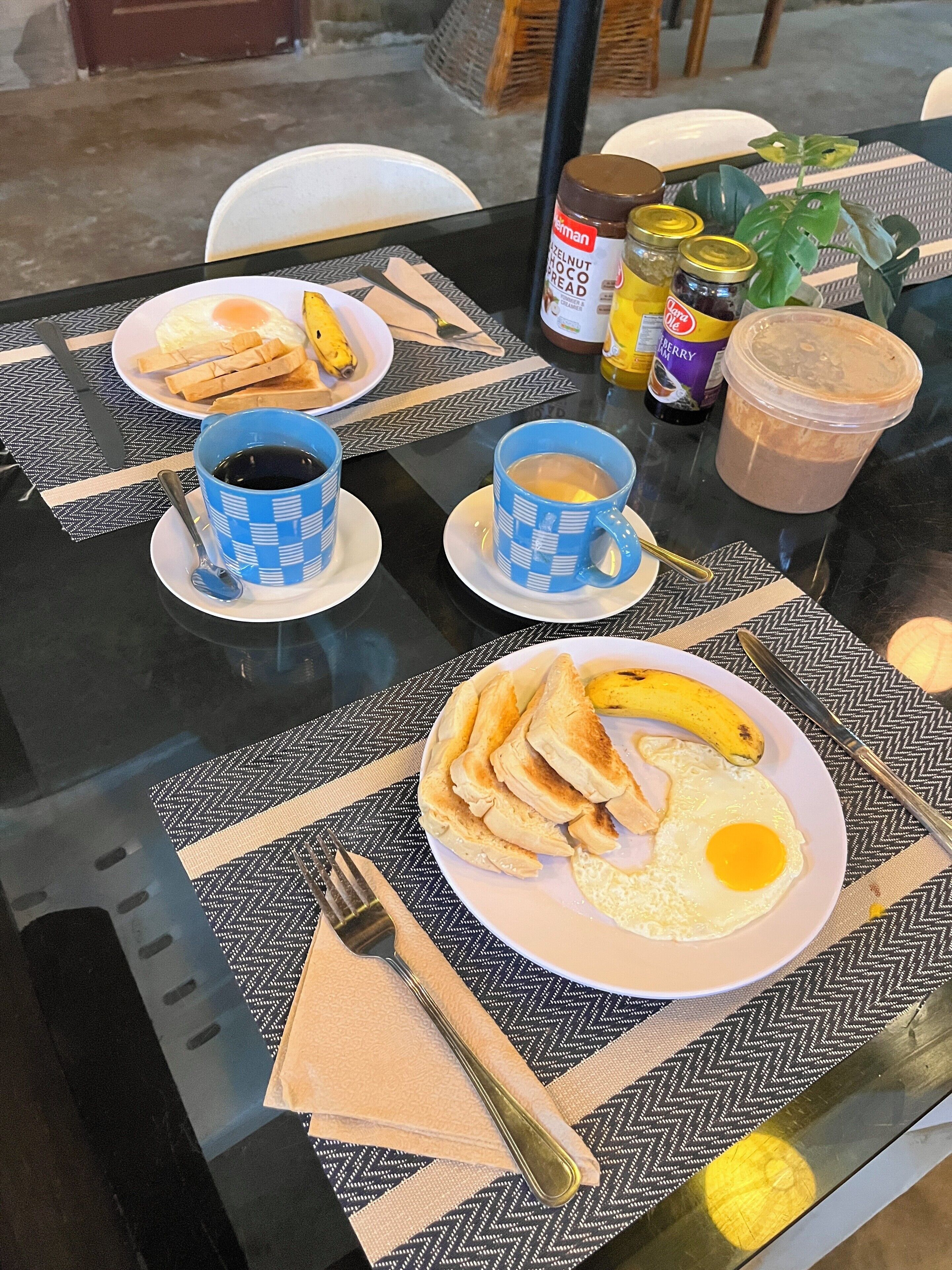 A breakfast table with plates of toast, eggs, and bananas, two cups of coffee, and condiments.