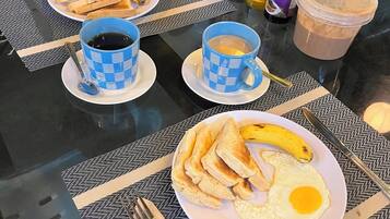 A breakfast table with plates of toast, eggs, and bananas, two cups of coffee, and condiments.