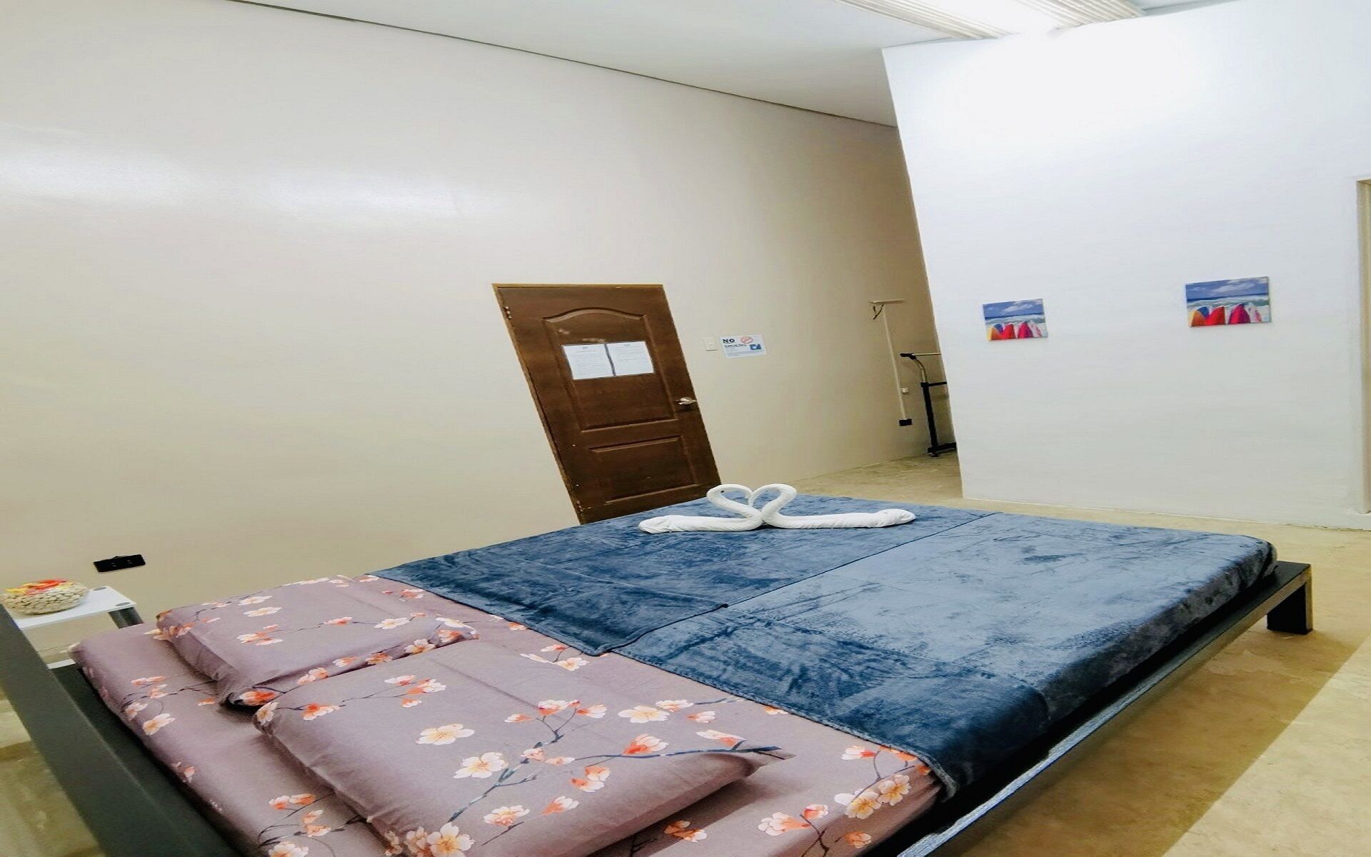 A bedroom with a bed, floral bedding, a door, and a wall with a picture.