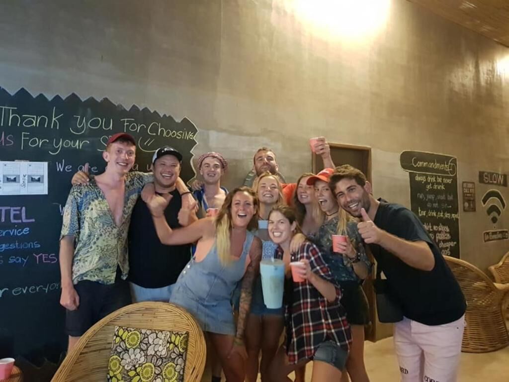 Eine Gruppe von Personen in ungezwungener Atmosphäre in einem Innenraum, an einer Tafel Botschaften stehen und ein Schild mit einer 'Gebots'-Anweisung für Gäste ist angebracht.