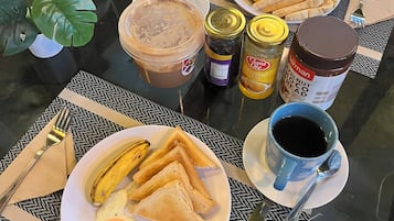 A breakfast table with plates of toast, eggs, and a banana, along with condiments and a coffee cup.