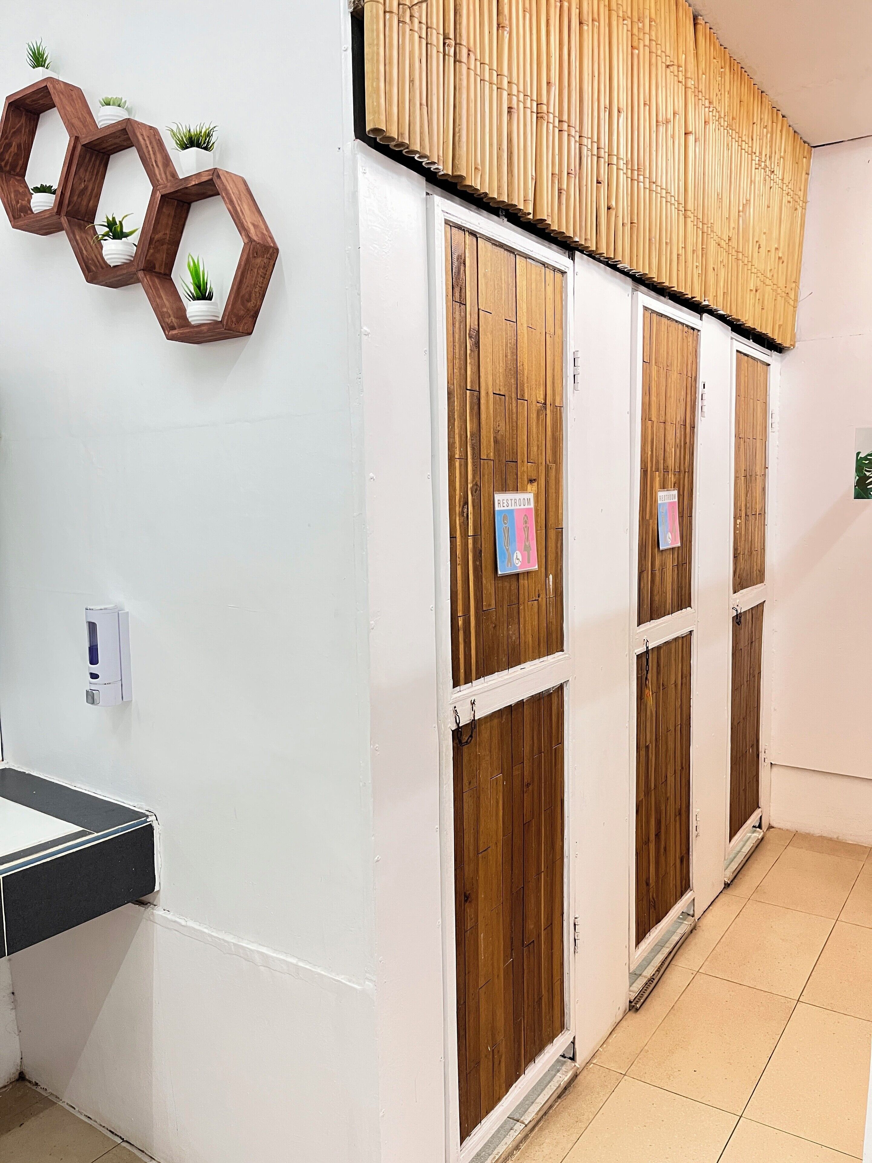 A restroom with wooden doors, a hand sanitizer dispenser, and hexagonal wooden shelves with potted plants.