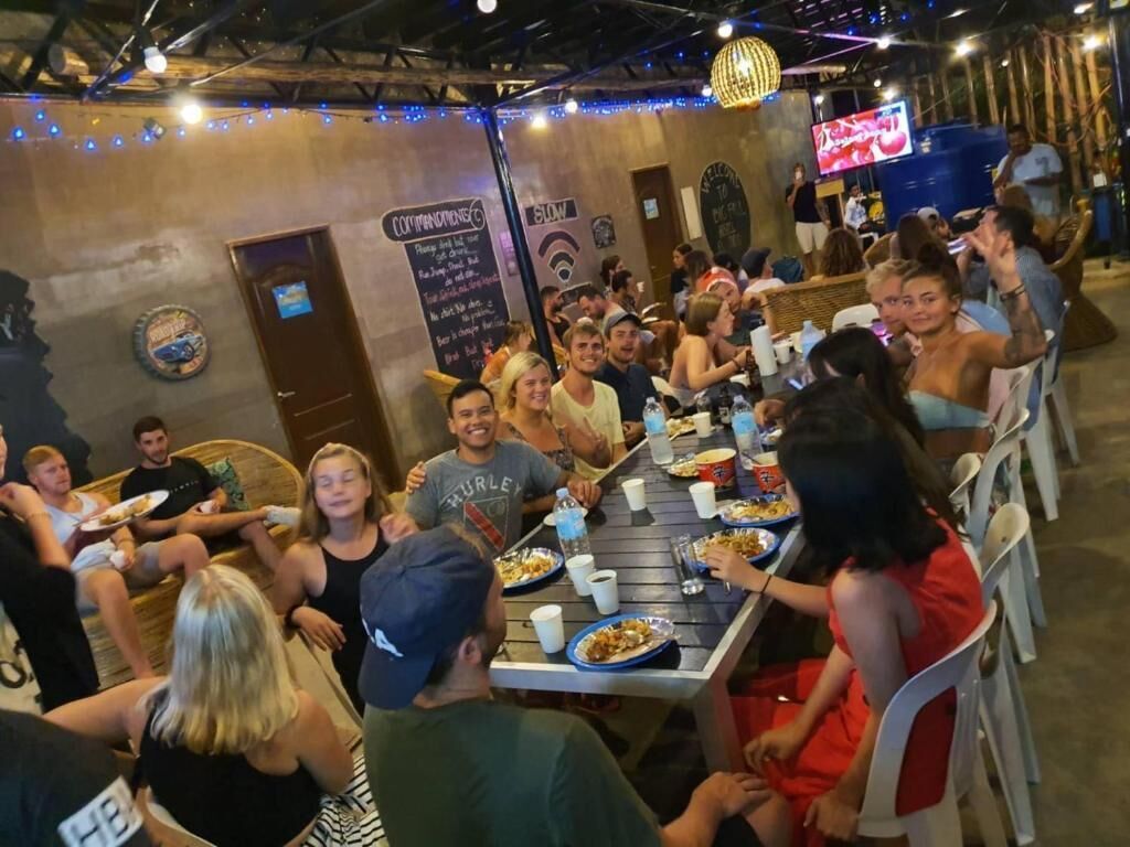 A group of people dining at a restaurant with a casual atmosphere, featuring a long communal table and individual seating.