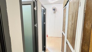Un couloir étroit, avec une porte-fenêtre coulissante sur la gauche, un mur recouvert de panneaux de bois sur la droite et un ventilateur de plafond au centre.