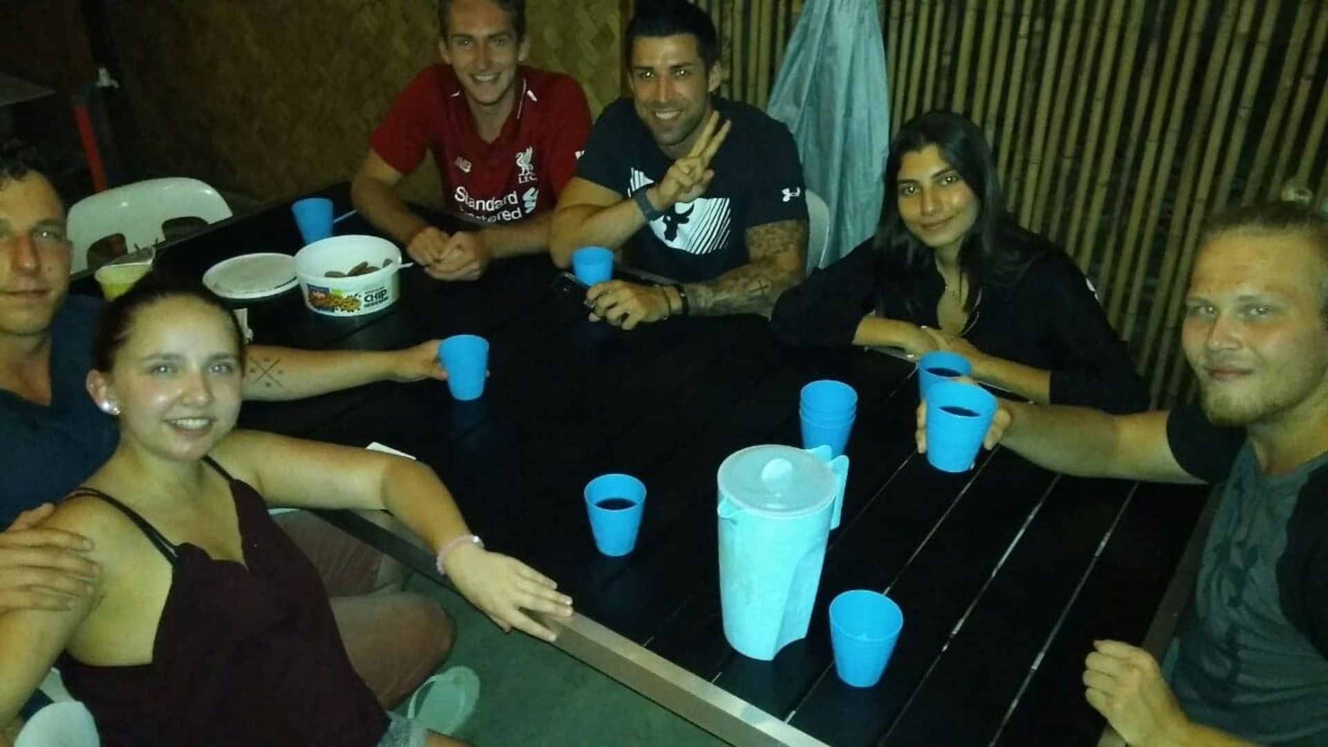 Um grupo de pessoas sentado à mesa, com copos de plástico azuis e uma tigela de petiscos.