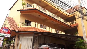 A multi-story building with balconies, a covered parking area, and a sign for a mini cost apartment and guesthouse. - Mini Cost Apartment & Guesthouse (Chiang Mai)