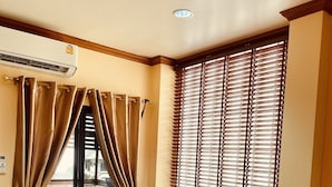 A room with a single bed, beige walls, a window with blinds, and an air conditioning unit. - Mini Cost Apartment & Guesthouse (Chiang Mai)