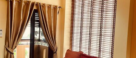 Une chambre avec un lit simple, des murs de couleur beige, une fenêtre avec des stores et un appareil de climatisation.