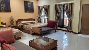 A hotel room with a large bed, a sofa, a small table, and a chair. There are curtains on the windows and a painting on the wall. - Mini Cost Apartment & Guesthouse (Chiang Mai)