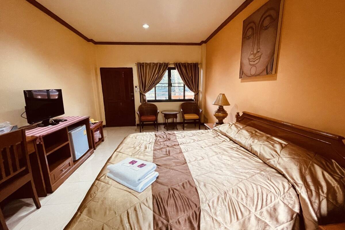 Ein Hotelzimmer mit einem großen Bett, einem Schreibtisch mit Fernseher, einem Sessel, einem kleinen Tisch und einem Fenster mit Vorhängen.
