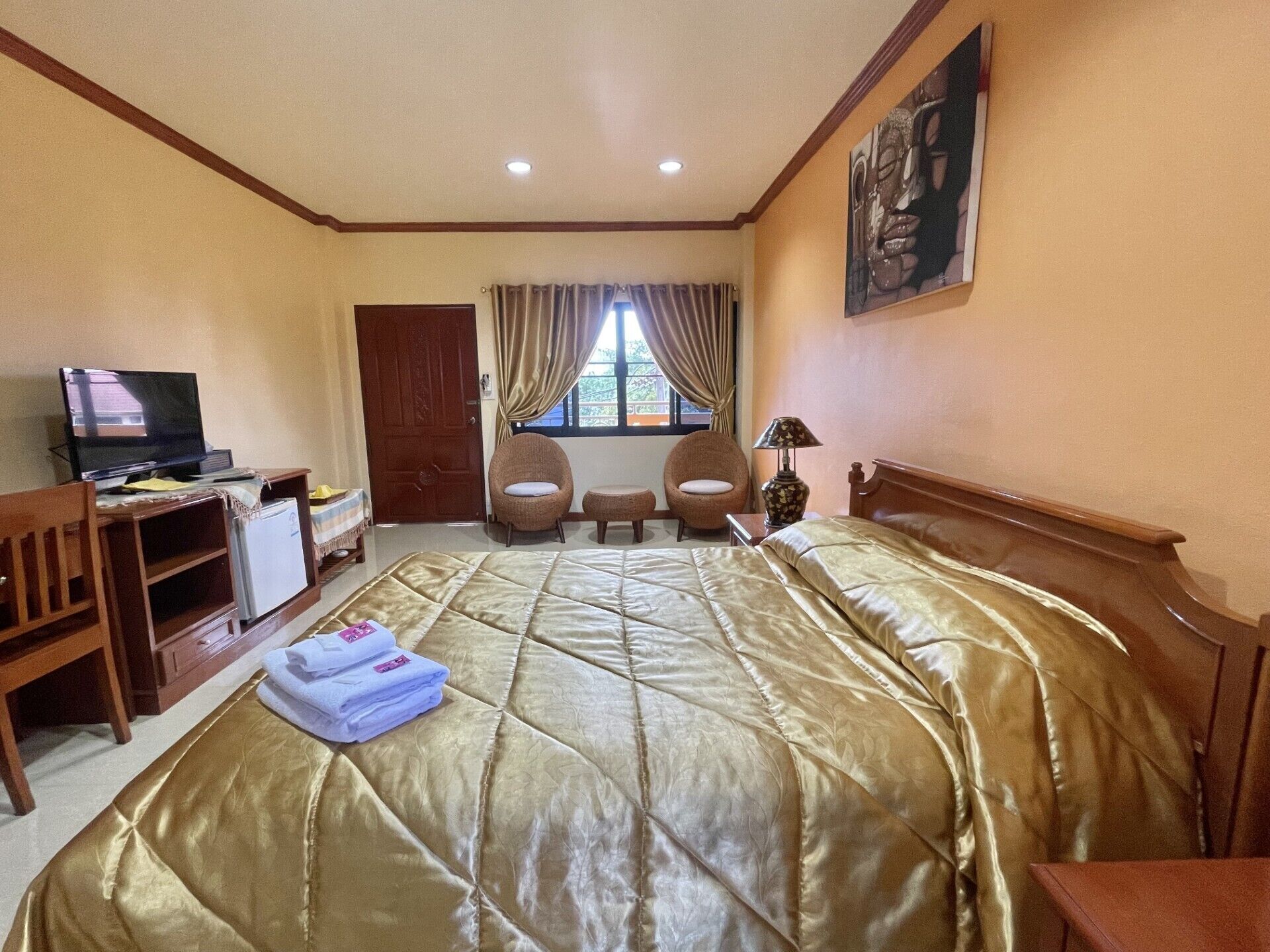 A hotel room with a large bed, a desk with a television, two armchairs, a small table with a lamp, and a painting on the wall.