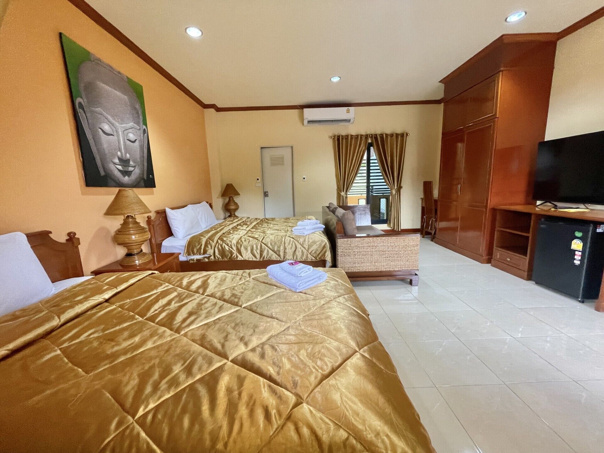 A hotel room with two beds, a television, a desk, and a large Buddha painting on the wall.